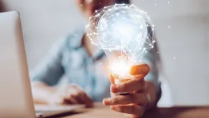 Picture of a person working on a computer and holding a bulb in the hand