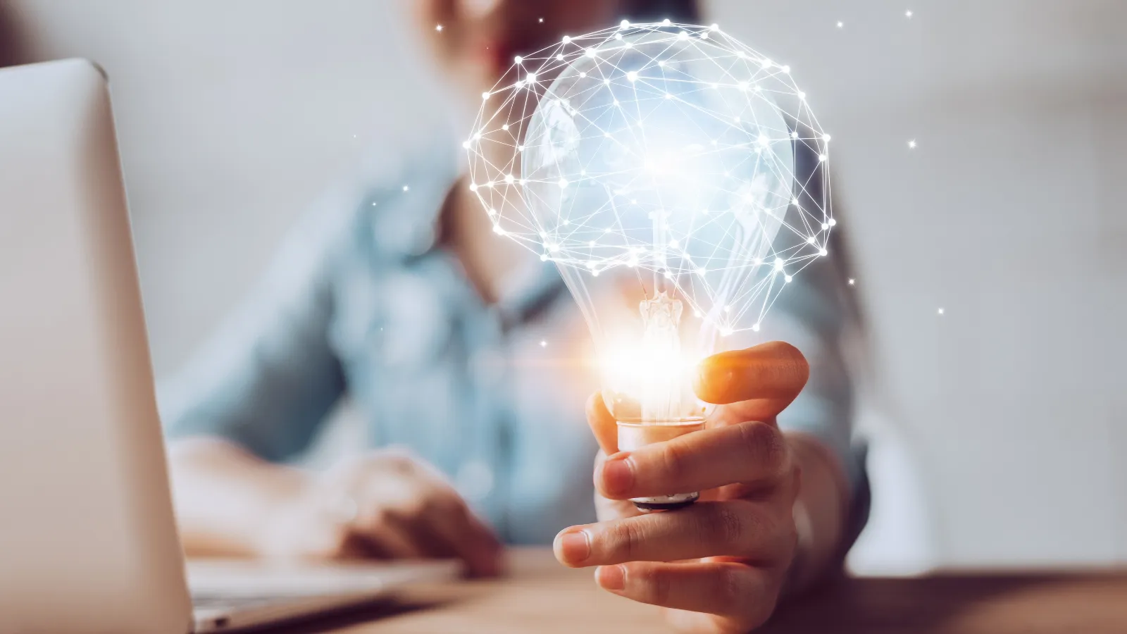Picture of a person working on a computer and holding a bulb in the hand